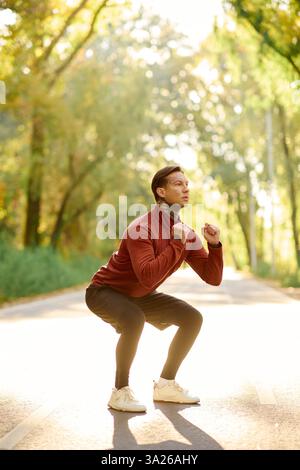 L'uomo tatuato fa degli squat eleganti su un tranquillo percorso naturalistico. Foto Stock