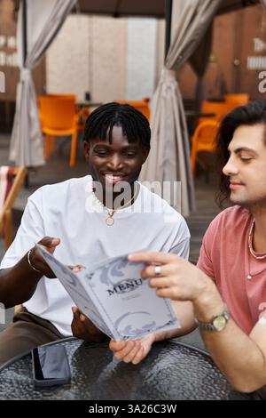 Una coppia gay amorevole condivide un momento di gioia mentre guarda il menu in un invitante Cafe'. Foto Stock