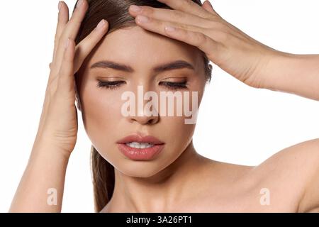 Una donna giovane e bella tocca la fronte in un momento rifrangente con uno stile elegante. Foto Stock