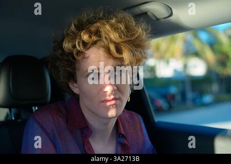 Una persona con i capelli ricci siede in un'auto che sembra contemplativa e la luce del sole getta ombre sul viso. Miami, Florida, Stati Uniti Foto Stock