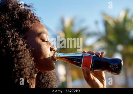 In una giornata di sole all'aperto, una donna gode di una bibita fredda da una bottiglia di vetro. Miami, Florida, Stati Uniti Foto Stock