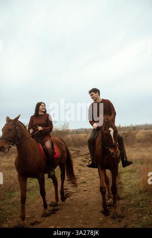 Giovani e innamorati, uomini e donne che cavalcano a cavallo attraversano un campo autunnale. Foto Stock