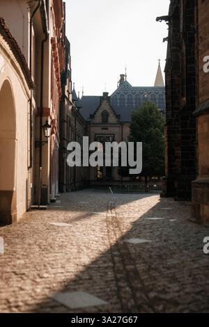 Praga, repubblica Ceca - 15 agosto 2023: Vicolo acciottolato che conduce all'edificio storico nel complesso del castello di praga, immerso nella luce del sole mattutino Foto Stock