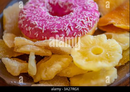 Una deliziosa gamma di spuntini mette in mostra una ciambella rosa vibrante con spruzzi accoccolati tra dolci croccanti e fette di ananas essiccato, perfetto per lo shar Foto Stock