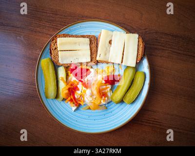 Una colazione colorata vi attende con uova perfettamente fritte accoccolate su un piatto insieme a croccanti cetrioli sottaceto e carote vivaci. Ad peperoncino rosso Foto Stock