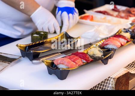 Lo chef sushi che indossa i guanti prepara il nigiri di tonno fresco al mercato del pesce di Tokyo, mentre le porzioni placcate con zenzero sottaceto sono disposte in tr decorativo Foto Stock