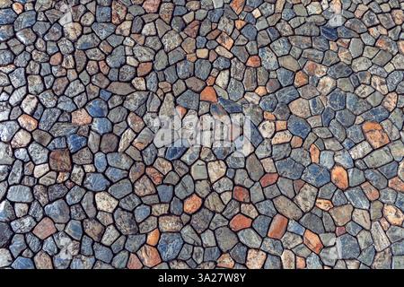Sfondo caratterizzato da un'antica pavimentazione in pietra composta da piccole e grandi pietre naturali in sfumature miste di terra strettamente unite tra loro creando un forte An Foto Stock