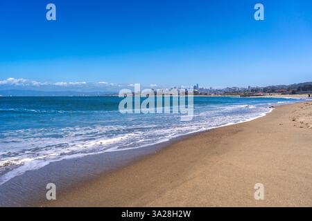 La spiaggia sabbiosa di Golden Gate Beach incontra l'Oceano Pacifico, con lo skyline di San Francisco visibile in lontananza sotto un cielo azzurro Foto Stock
