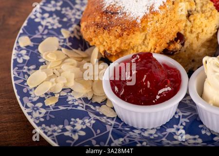 Uno Scone di mandorle di ciliegia con marmellata di fragole . La gelatina si trova in una ciotola bianca di panna coagulata Foto Stock