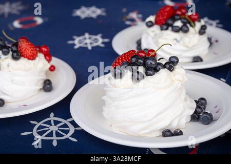 Mini torta Pavlova con fragola, mirtillo e ribes rosso su sfondo scuro. Dessert a base di meringa. Mini Pavlova con fragole e mirtilli. Foto Stock