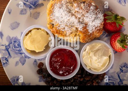 Un piatto di cibo con scone con tè alla panna e condimenti. Il dessert è uno scone con sopra zucchero a velo. I condimenti includono marmellata di fragole e bu Foto Stock