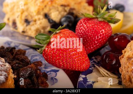 Un piatto di cibo con sopra una fragola. Il piatto è blu e bianco. Sul piatto ci sono altri tipi di frutta e pasticcini Foto Stock