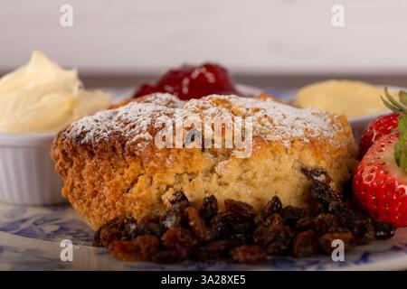 Un piatto di scone alla frutta con una fragola sopra. Il piatto è ricoperto da una salsa bianca e una ciotola bianca Foto Stock
