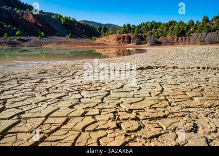 Un lago artificiale parzialmente essiccato in una cava abbandonata di Evia, Grecia, caratterizzato da terra incrinata, scogliere erose e arido, alberi senza foglie sotto una c Foto Stock