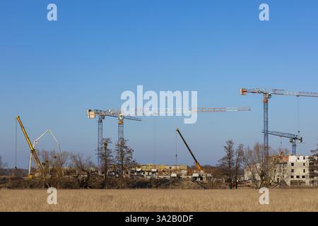 Wroclaw, Polonia - 24 febbraio 2025: Gru a torre e attrezzature per la costruzione che lavorano su un progetto di costruzione su larga scala in un paesaggio rurale Foto Stock
