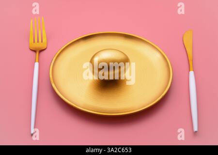 Seduto su un piatto dorato, un uovo dorato brilla accanto a lussuose posate su un vivace sfondo rosa, che rappresenta la ricchezza e l'opportunità di investimento Foto Stock