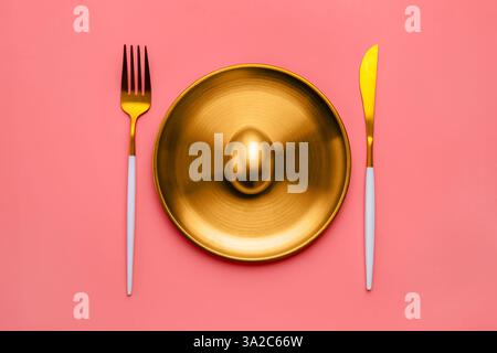 Seduto su un piatto dorato, un uovo dorato brilla accanto a lussuose posate su un vivace sfondo rosa, che rappresenta la ricchezza e l'opportunità di investimento Foto Stock