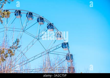 La ruota panoramica con cabine vuote offre viste mozzafiato sul parco divertimenti, promettendo un emozionante giro sotto la vasta distesa di un blu vibrante Foto Stock