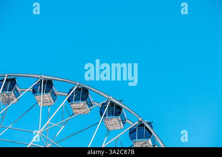 La ruota panoramica con cabine vuote offre viste mozzafiato sul parco divertimenti, promettendo un emozionante giro sotto la vasta distesa di un blu vibrante Foto Stock