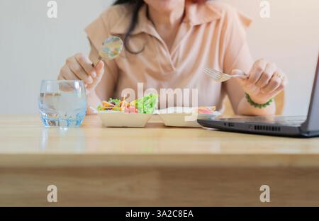 Colpo ritagliato di nutrizionista donna con cibo sano che lavora su notebook al tavolo in ufficio. Messa a fuoco selettiva. Foto Stock