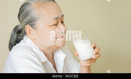 Le mani di una donna anziana che tiene un bicchiere di latte. Felice donna anziana che si diverte mentre beve latte a casa. Vista laterale. Foto Stock