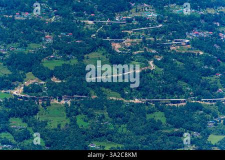 Vista panoramica di una strada serpentina che si snoda attraverso un'area collinare verdeggiante, circondata da fitte vegetazione e punteggiata da piccoli edifici, catturando un tranq Foto Stock