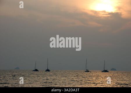 Uno splendido tramonto sul mare calmo di Ao Nang Beach, Thailandia, con barche che galleggiano sull'acqua e isole lontane che creano una silhouette mozzafiato Foto Stock