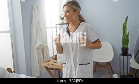 Donna sorridente in una spa che indossa un'uniforme bianca con un taglio di capelli moderno ed elegante, in piedi in una stanza luminosa e ben illuminata con un'atmosfera rilassante Foto Stock