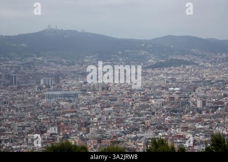 Vista sopraelevata del paesaggio urbano di Barcellona con la collina Tibidabo. Paesaggio urbano, edifici densi e atmosfera nebulosa Foto Stock