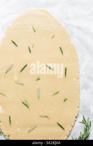 Vista dall'alto dell'impasto arrotolato con zucchero al rosmarino, processo di preparazione dei biscotti con zucchero tagliato Foto Stock