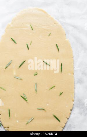 Vista dall'alto dell'impasto arrotolato con zucchero al rosmarino, processo di preparazione dei biscotti con zucchero tagliato Foto Stock