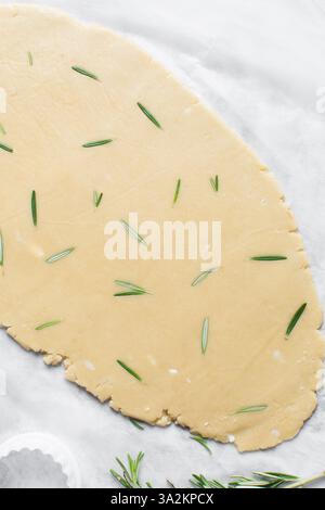 Vista dall'alto dell'impasto arrotolato con zucchero al rosmarino, processo di preparazione dei biscotti con zucchero tagliato Foto Stock