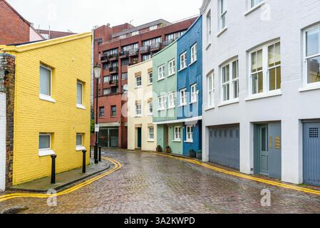 Case cittadine dai colori pastello lungo una stretta strada acciottolata a Londra in una giornata invernale piovosa Foto Stock