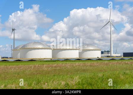 Grande tansk di combustibile circondato da pannelli solari e turbine eoliche in un'area portuale in una soleggiata giornata estiva Foto Stock