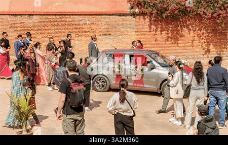 Dunbar Square, Bhaktapur, Nepal - 10 febbraio 2025 - Una processione di ospiti nuziali a seguito di un'auto per matrimoni con spettatori in attesa Foto Stock