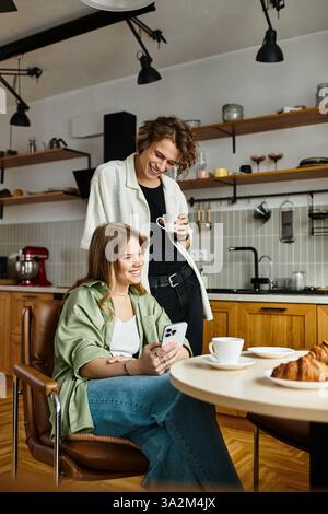 Due partner condividono un momento di gioia a casa, gustando caffè e pasticcini mentre si connettono. Foto Stock