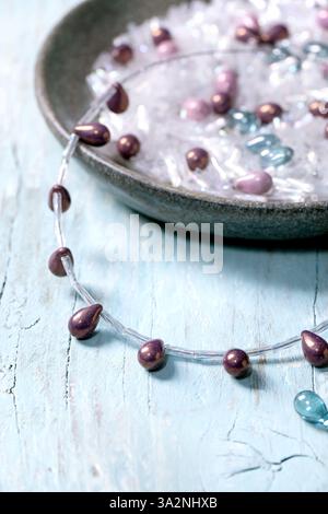 Creazione di gioielli fatti a mano. Creazione di collana con perline in vetro e componenti in una ciotola in ceramica su sfondo di legno chiaro. Concetto di hobby fai da te. Chiudi Foto Stock