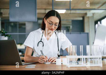 Scrittura da parte di utilizzando una penna. Medico donna in giacca bianca è al chiuso. Foto Stock