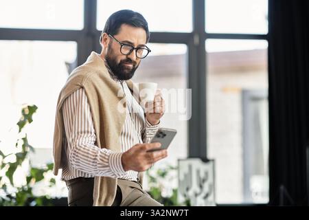 Il bel signore anziano sorseggia un caffè e interagisce con il suo smartphone in un ambiente accogliente. Foto Stock