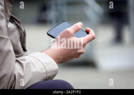 Smartphone nelle mani di un uomo seduto sulla strada della città. Guardare video e giocare all'aperto Foto Stock