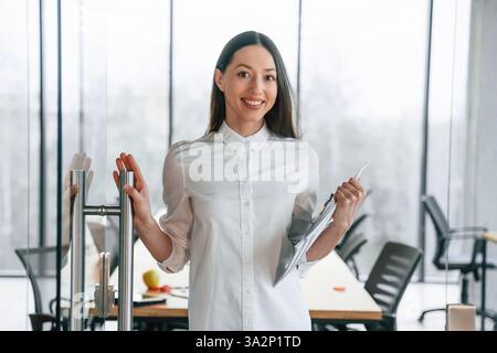 Stare in piedi e tenere in mano i documenti. Una donna d'affari è al chiuso in ufficio. Foto Stock