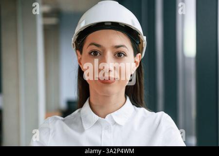 Ritratto di architetto donna che è in elmetto e in abiti bianchi al chiuso. Foto Stock
