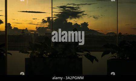 Vista della pista dell'aereo dall'interno della finestra dell'aeroporto, con il tramonto sullo sfondo Foto Stock