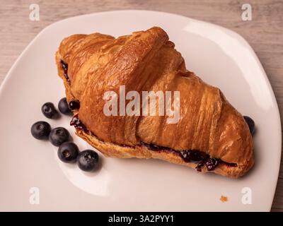 Croissant con marmellata e mirtilli freschi su piatto bianco. Primo piano. Foto Stock