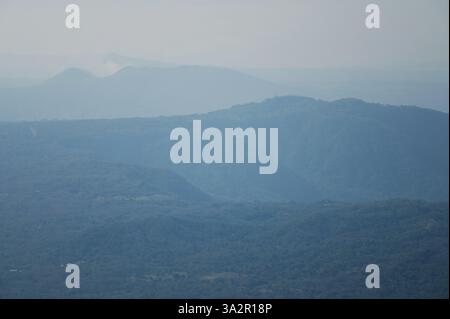 I morbidi strati blu delle montagne creano un paesaggio sereno sotto un cielo nebbioso alla luce del pomeriggio. Foto Stock