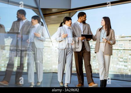 Tre colleghi si riuniscono in un ufficio luminoso, partecipando a una discussione mentre esaminano un tablet insieme. L'atmosfera è piena di creatività Foto Stock