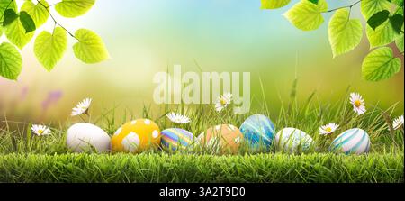 Sette uova di pasqua dipinte che celebrano una felice Pasqua in una giornata primaverile con un prato erboso verde, luce solare intensa, foglie di alberi e uno sfondo caldo. Foto Stock