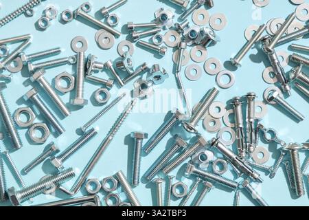 Diversi bulloni filettati e dadi cromati su sfondo blu Foto Stock