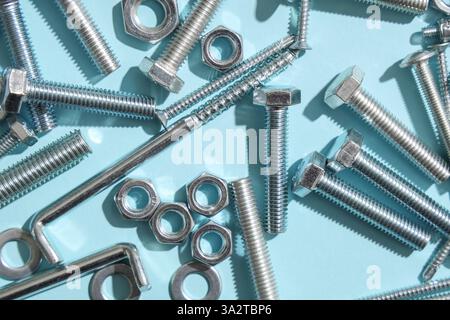 Diversi bulloni filettati e dadi cromati su sfondo blu Foto Stock