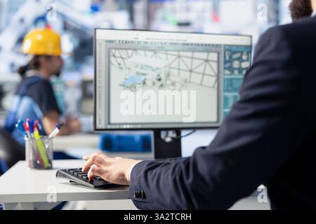 Il lavoratore della fabbrica fotovoltaica che programma macchinari per la produzione di energia solare tramite PC, definisce le impostazioni del sistema per la massima efficienza. L'ingegnere lavora sull'assemblaggio di pannelli solari su workstation, primo piano Foto Stock